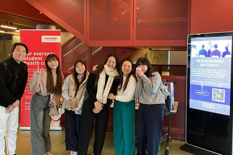 A group of international students smile and pose in a bright modern foyer