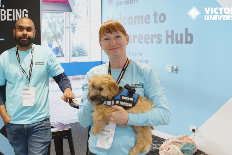 VU Open Day featuring a member of the student wellbeing team, as well as Heather holding Clover and smiling at the camera