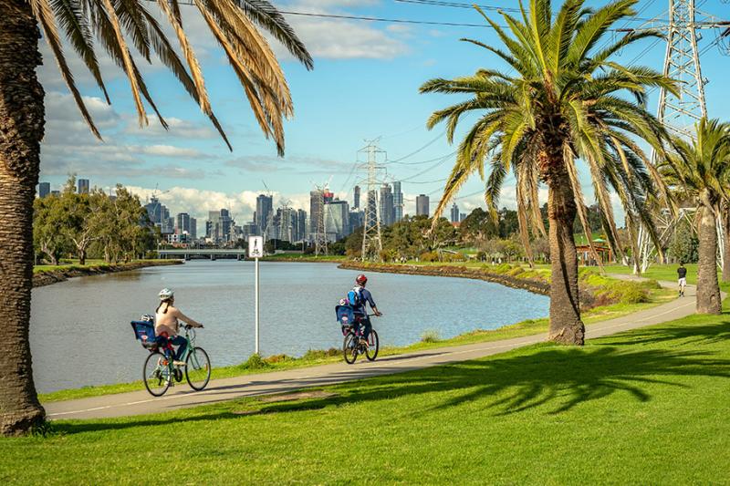 A family bikes along a riverside path, with a cityscape in the background