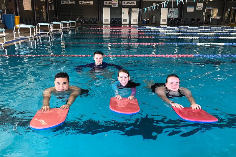 three young adult swimmers learning to swim using flutter boards