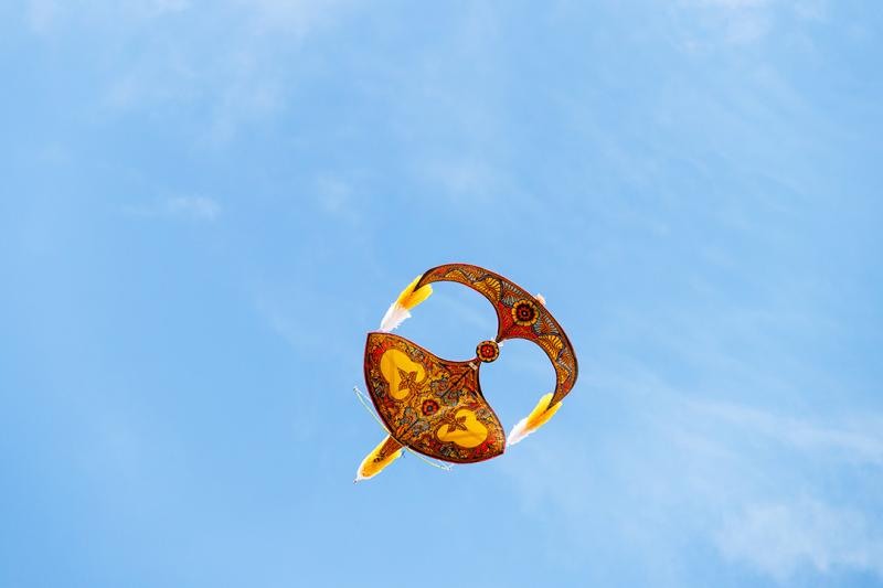 A gold kite in the shape of a malaysian mask in a blue sky