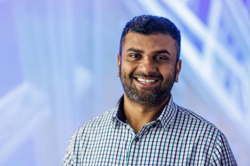 Professor Malindu Sandanayake smiling at the camera in front of an abstract image of a construction site 