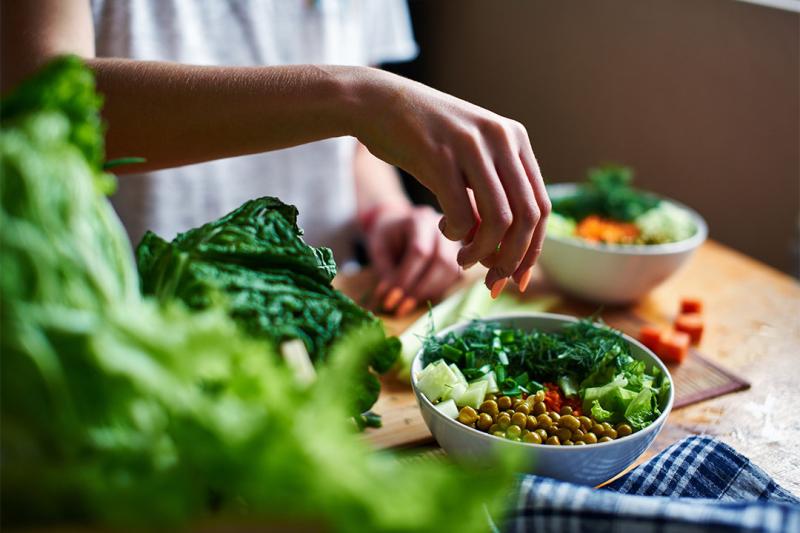 A healthy bowl of food being prepared by a person with orange painted fingernails.