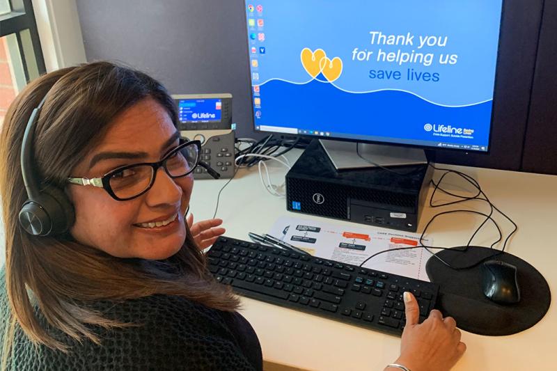 Kay Bajwa sitting in front of a computer at volunteering at Lifeline Western Melbourne, reading to answer calls.