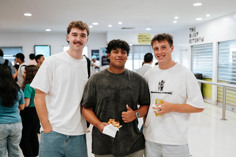 Three young men in a bright foyer with a cafe