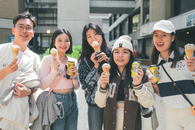 Students standing outside, holding an ice-cream and soft drink and smiling at camera.