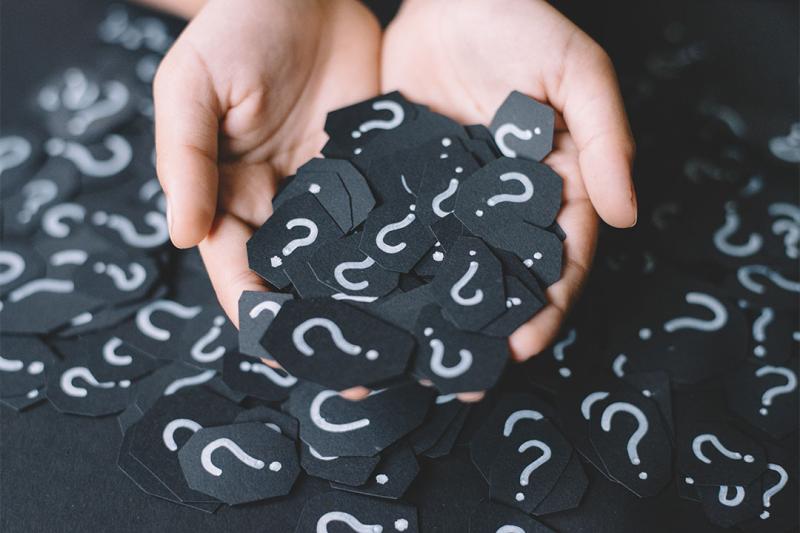 Hand holding small black cards with white question marks on it.