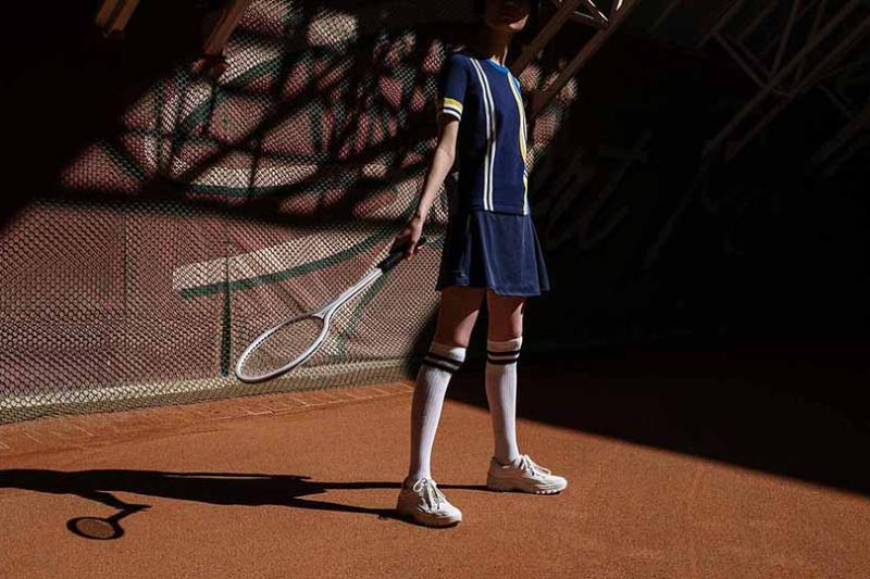 A tennis player stands on a clay court holding a racquet.