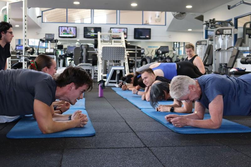 A group of people doing crunches on a yoga mat in a gym.