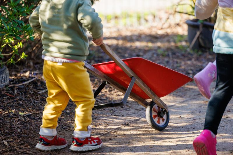 Unidentifiable children playing with a toy wheelbarrow at a childcare centre in Victoria.