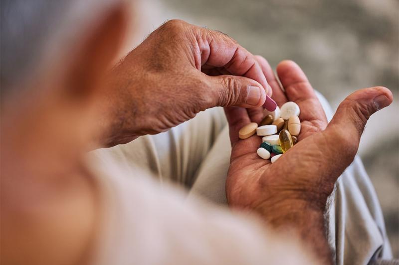 Hand holding a collection of different pills, to address chronic diease.