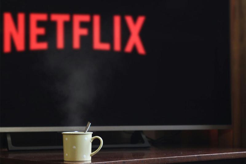 A coffee cup sits on a TV unit in front of a TV with the Netflix logo on it.