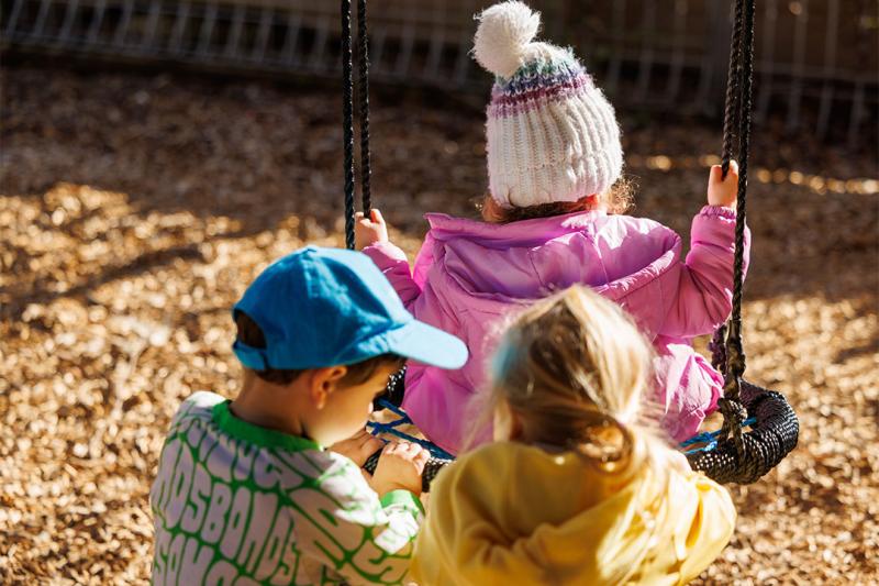 Three children play on a swing outside at a childcare centre.