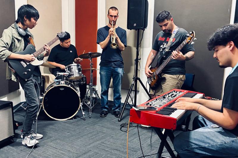 VU students playing musical instruments (keyboard, drums, guitars and trumpet) together.