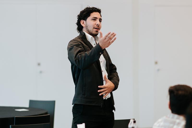 A young man in professional dress presents during a workshop