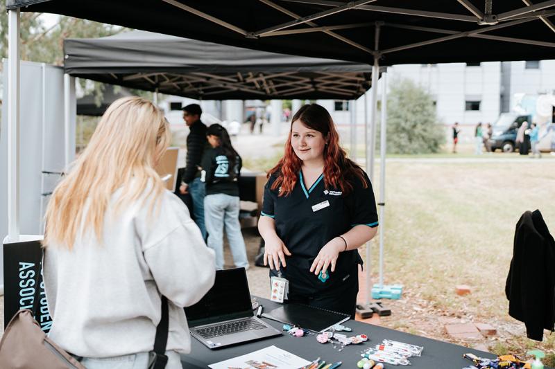 A young woman in a Victoria University polo shirt helps someone at an information stall