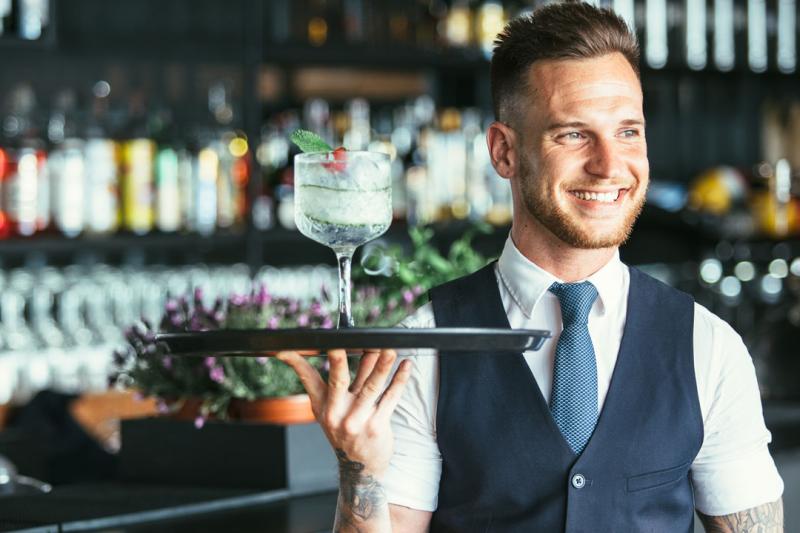 A bar employee holding a cocktail on a serving plate.