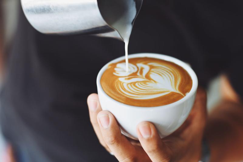 A person pouring steamed milk into a coffee cop, making latte art.