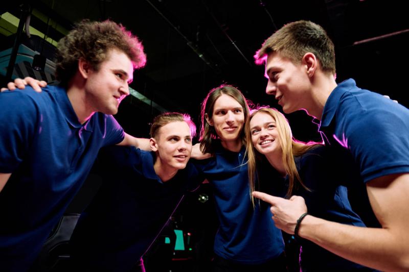 A group of students in an arcade huddling together. One person is speaking and pointing, the rest of the students are looking at him.
