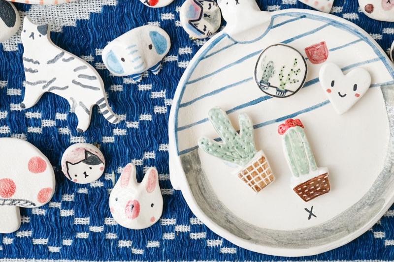 A collection of handmade clay magnets sitting on top a blue sewn fabric.