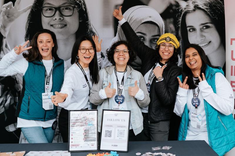 Five women standing at a VU Open Day stall promoting the Women in Tech group.