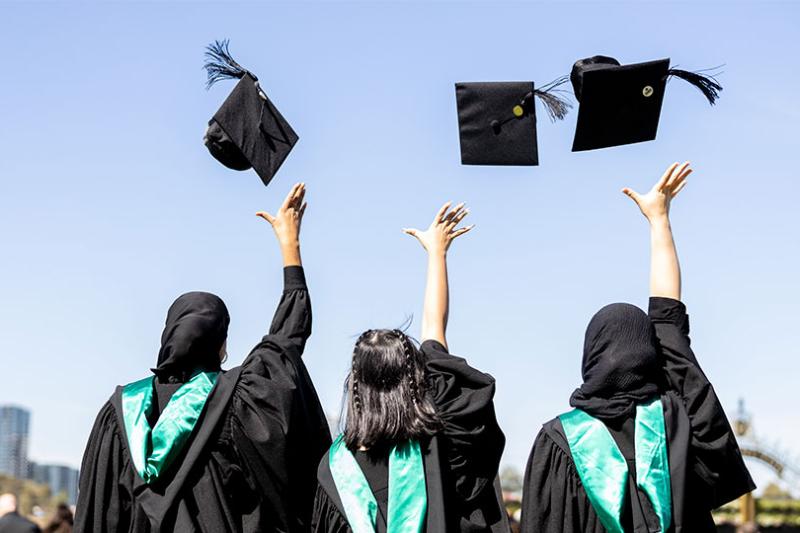Three graduates throw their caps in the air joyously after their graduation ceremony