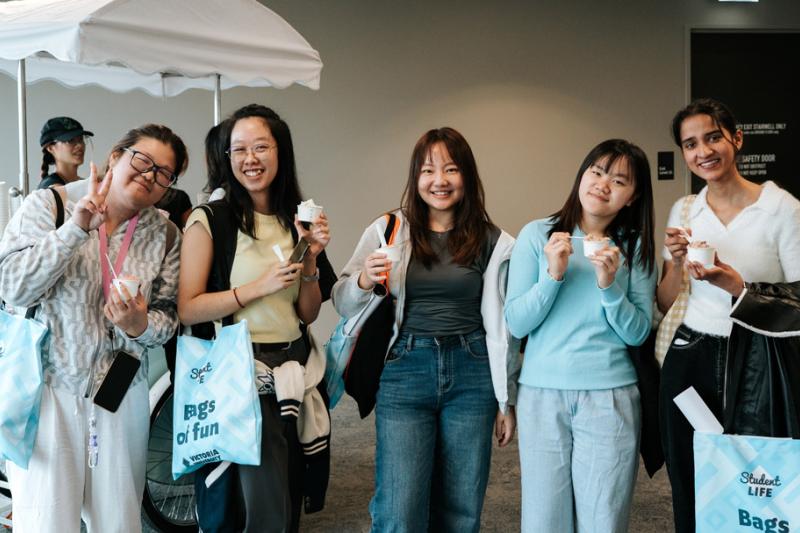 A group of students pose in front of an icecream cart with blue Victoria University tote bags