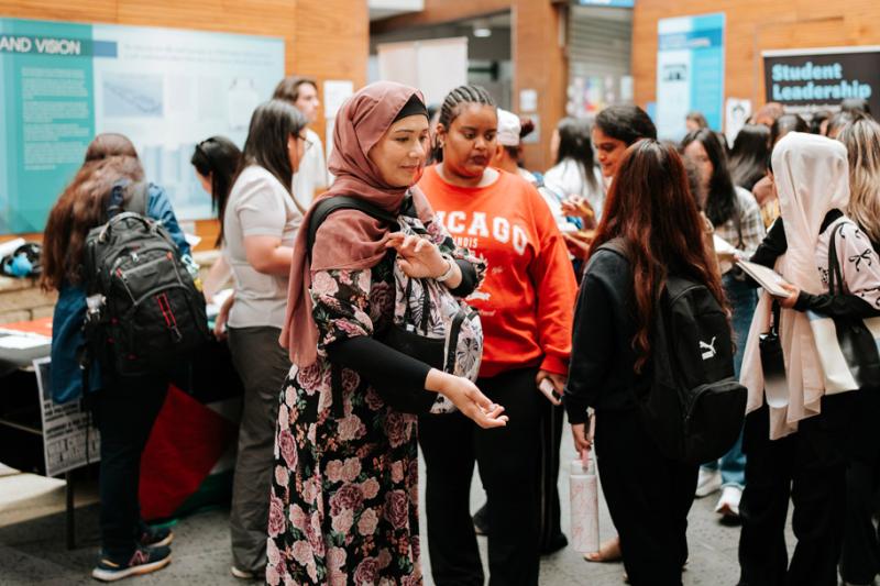 A large multicultural group of students interact with information stalls
