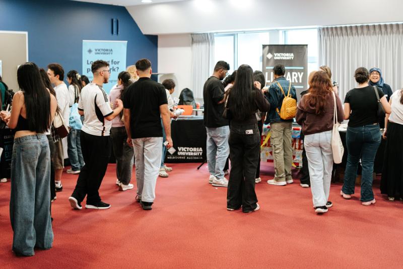 A large group of students mill around a room with Victoria Univerity signage and stalls