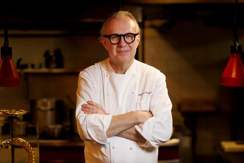 A middle aged man in a white chef jacket and horn-rimmed glasses in a country kitchen