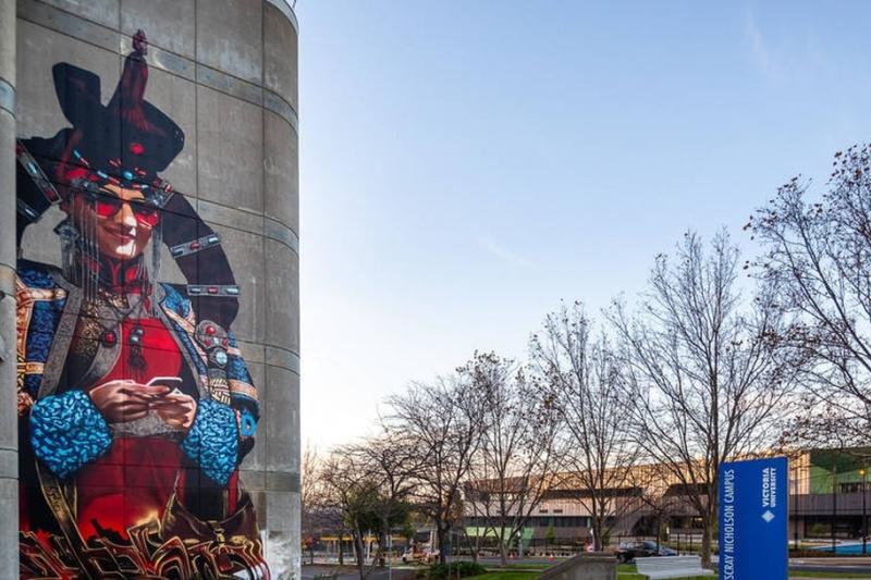 Colourful mural of a person on the side of a building with sky and trees to the side