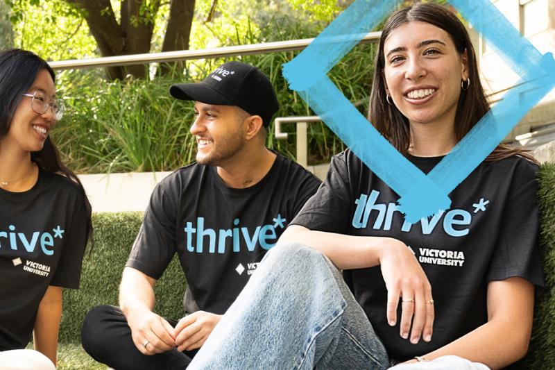 Three people are seated outside, smiling and chatting, wearing black t-shirts with 'Thrive' slogan. 