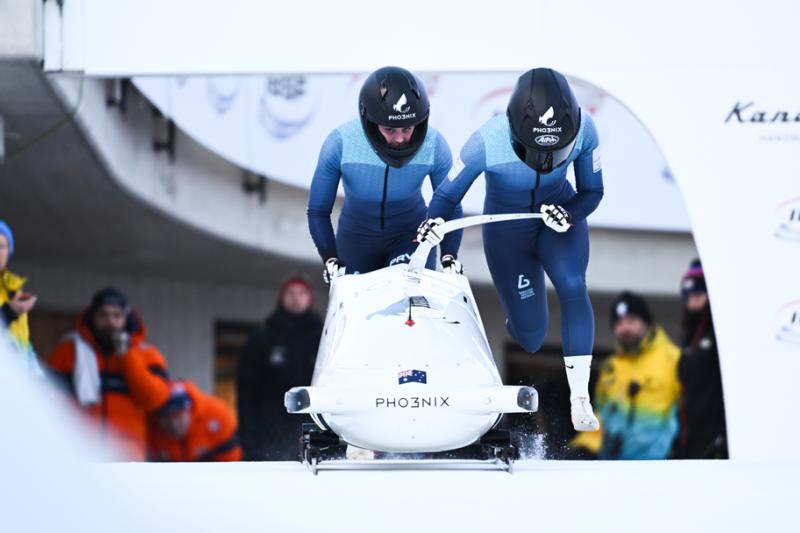 A two-person bobsleigh team taking off in full gear and helmets