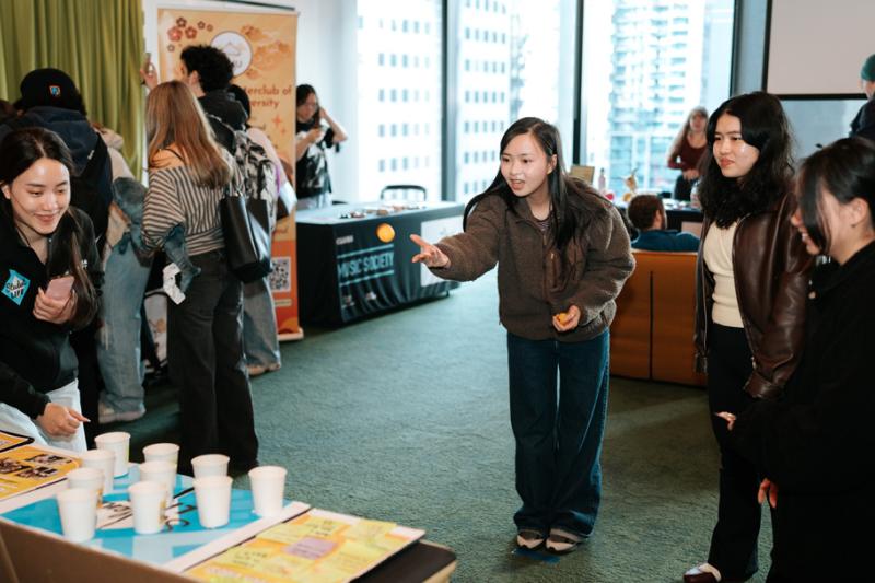 A group of students play a game of throwing balls into paper cups at a university event in a highrise building