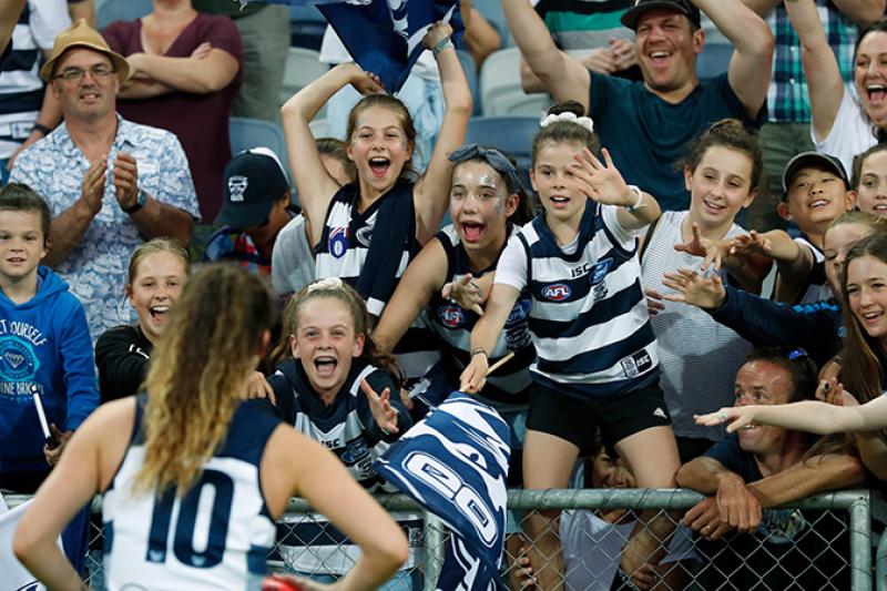 crowd including young girls in footy uniforms cheering