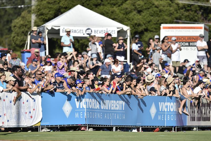 AFL crowd behind a Victoria University logo barrier