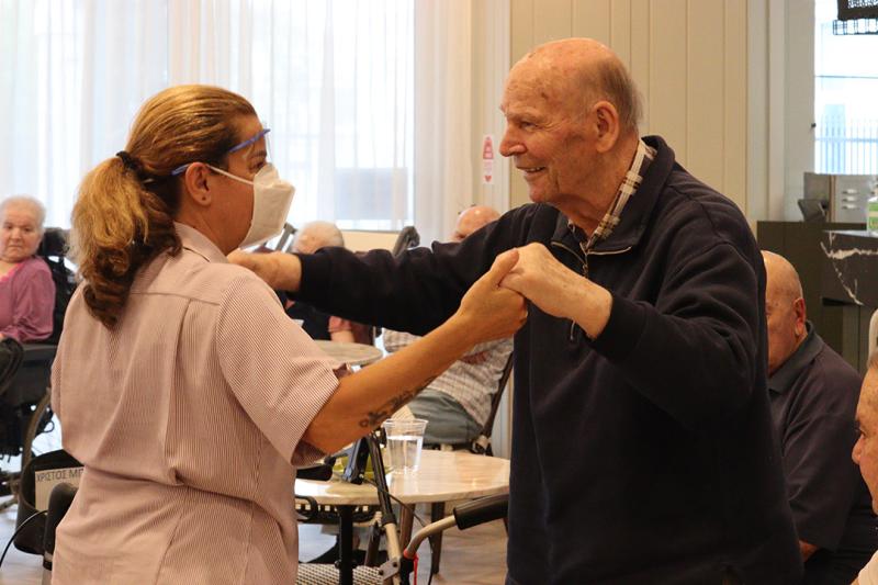 An elderly man dances with a carer