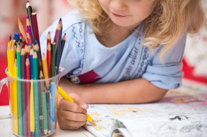  Blonde child colouring in with a jar full of colourful pencils.