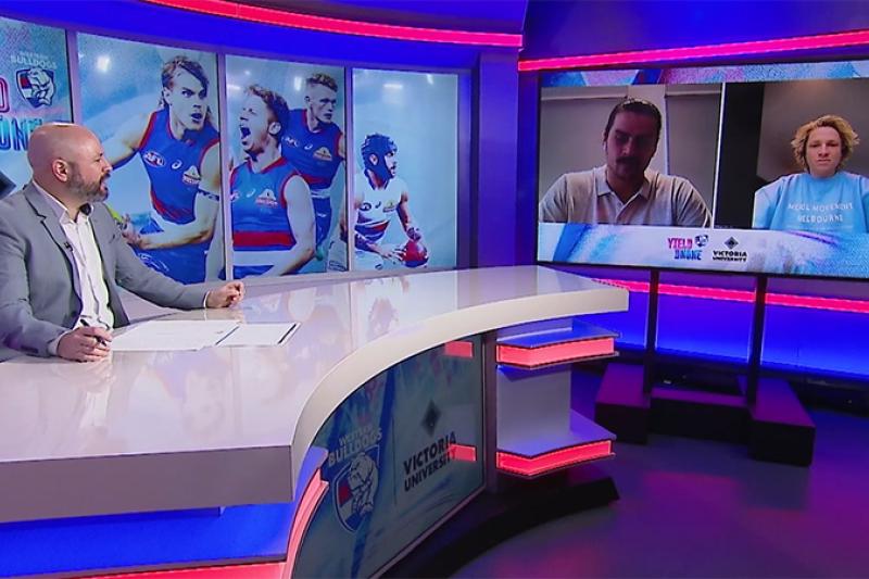 Male TV presenter at desk with Bulldogs colours and images talks to men on screen