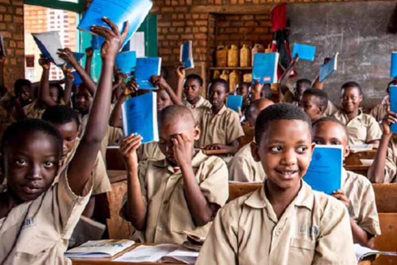 Group of Afrtican school children, in class, wearing uniforms, smiling and holding books