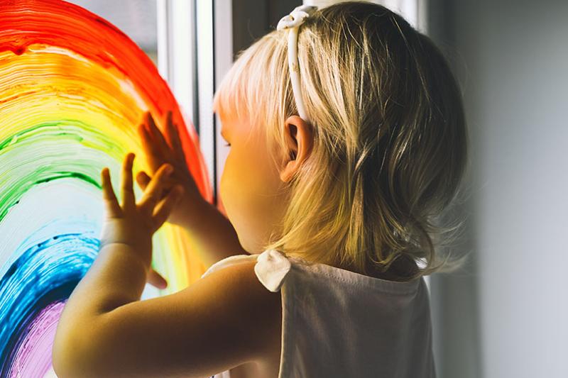Child fingerpainting a rainbow onto a window.