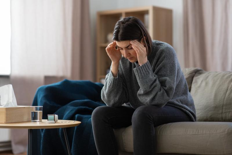  woman depressed on couch, holding head with pill bottle in front of her