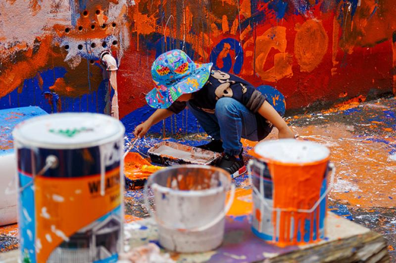 toddler painting an outdoor wall in bright colours