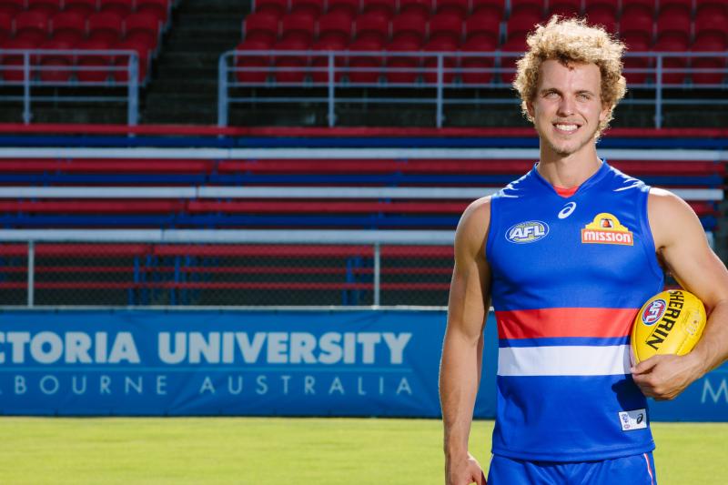  Mitch Wallis in his Bulldogs gear stands in front of a VU banner