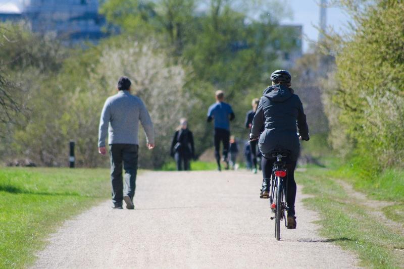  People in winter clothes walking and riding a bike in a park.