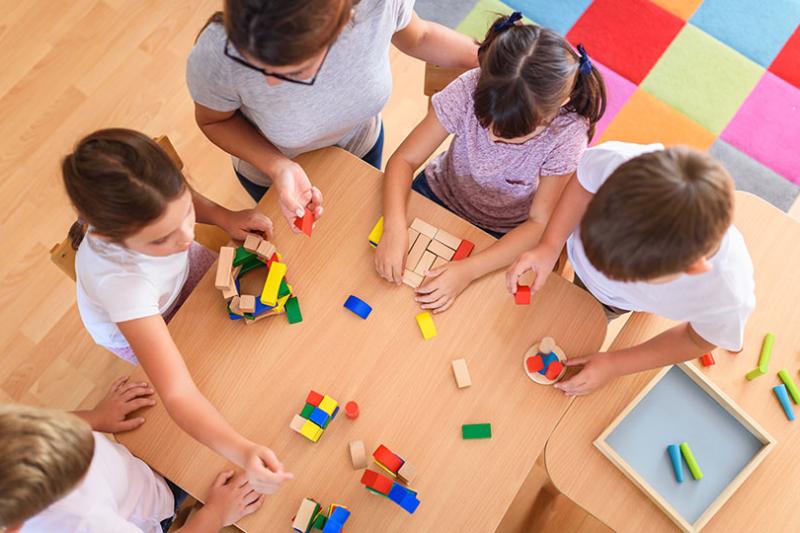  Preschool children sitting at a table playing with wooden toys.