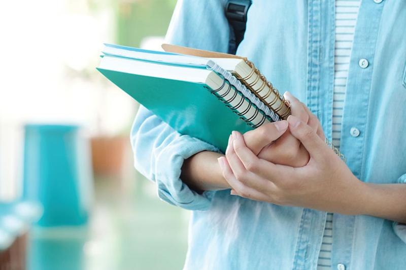  Student in blue shirt holds exercise books.