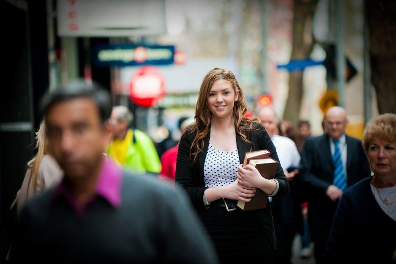 Student in busy city lane holding books and dressed professionally