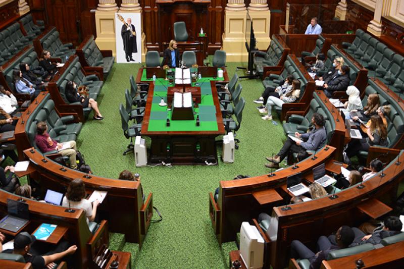 A stately looking room from above with curved wooden seating, with young people in seats