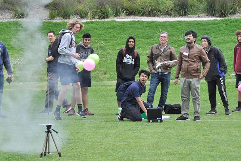 Young men watch a smoking mini launch pad
